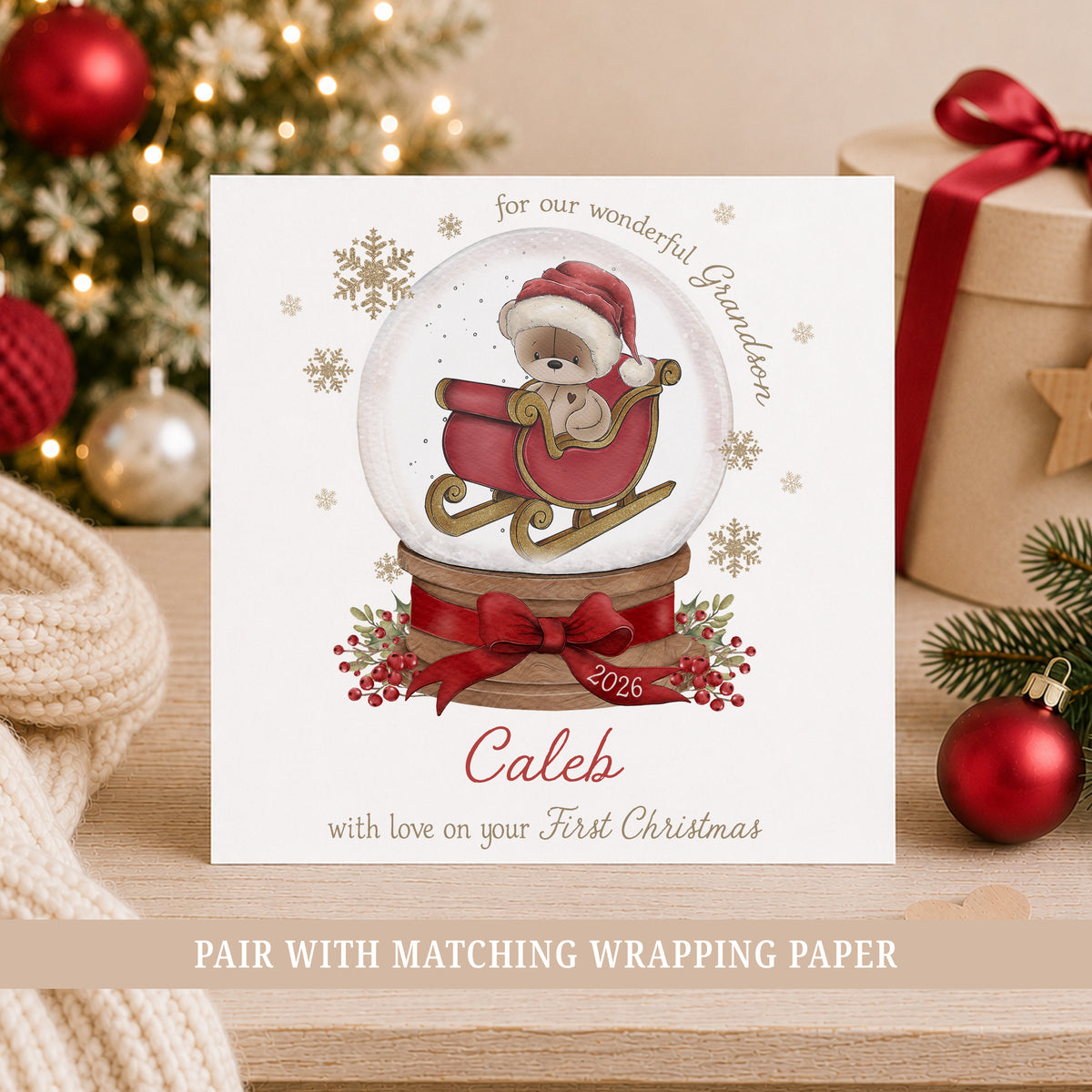 Personalised Grandson First Christmas card featuring a teddy bear in a red sleigh inside a Christmas snow globe, with red bow, berries and gold snowflakes. Personalised with a name and relation and also suitable for Son, Nephew or Godson.