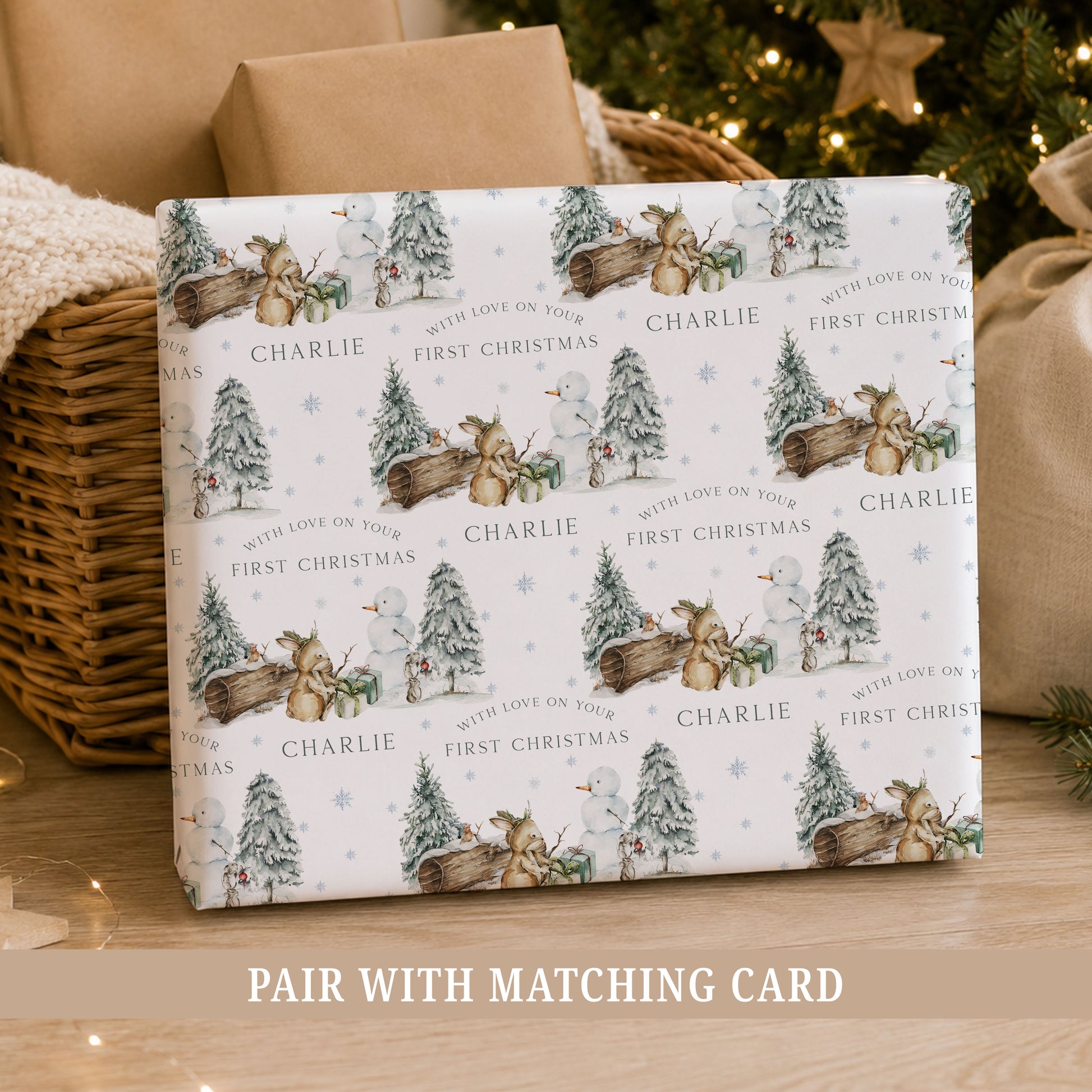 Personalised Baby Boy First Christmas wrapping paper featuring a winter woodland scene with a bunny, snowman, snowy Christmas trees and presents.