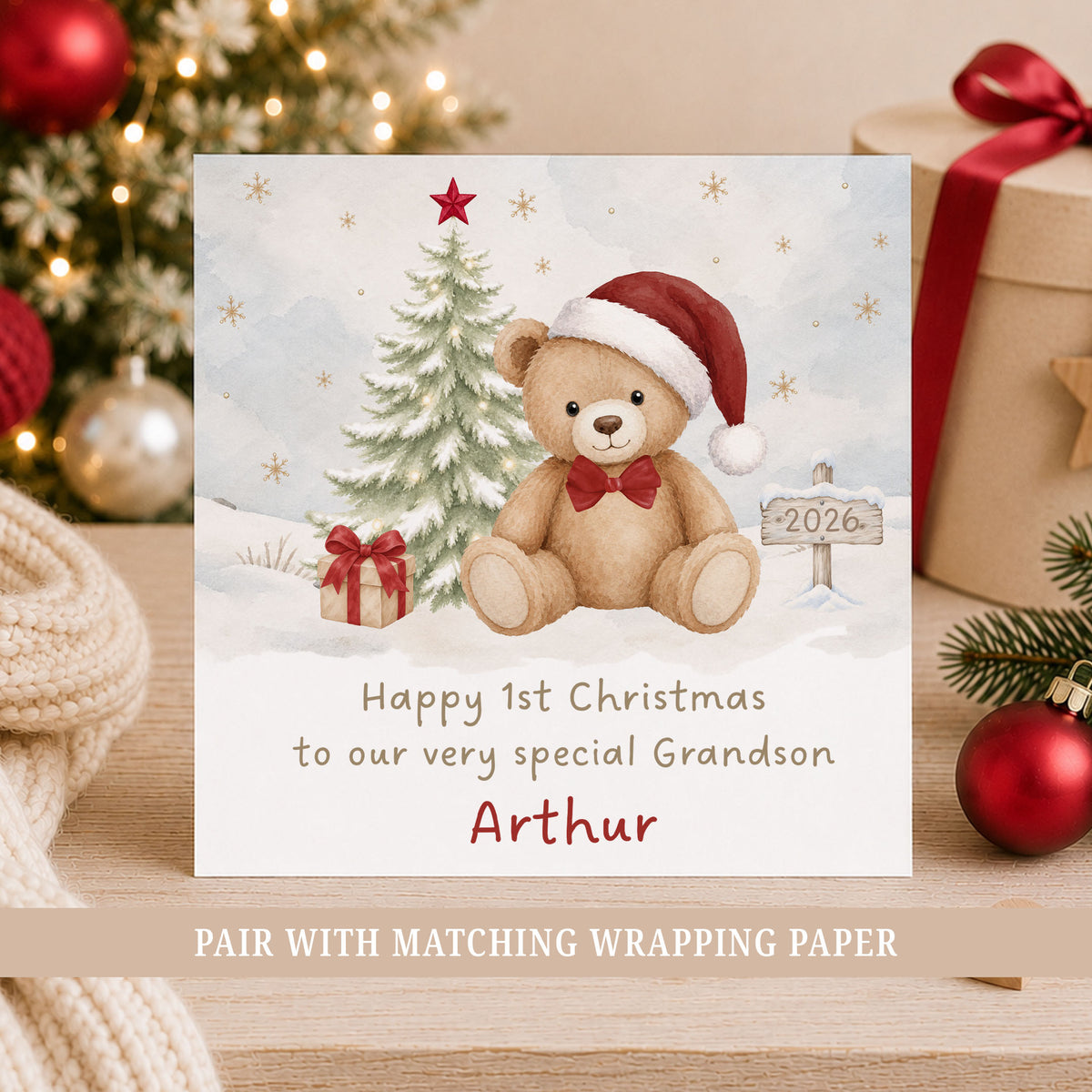 Personalised Grandson First Christmas card featuring a cute teddy bear wearing a red Santa hat and bow tie beside a snow-covered Christmas tree, wrapped present and 2026 sign. Personalised baby boy's 1st Christmas greeting card with name and relation, suitable for Grandson, Son, Nephew, Godson or a little boy celebrating his first Christmas.