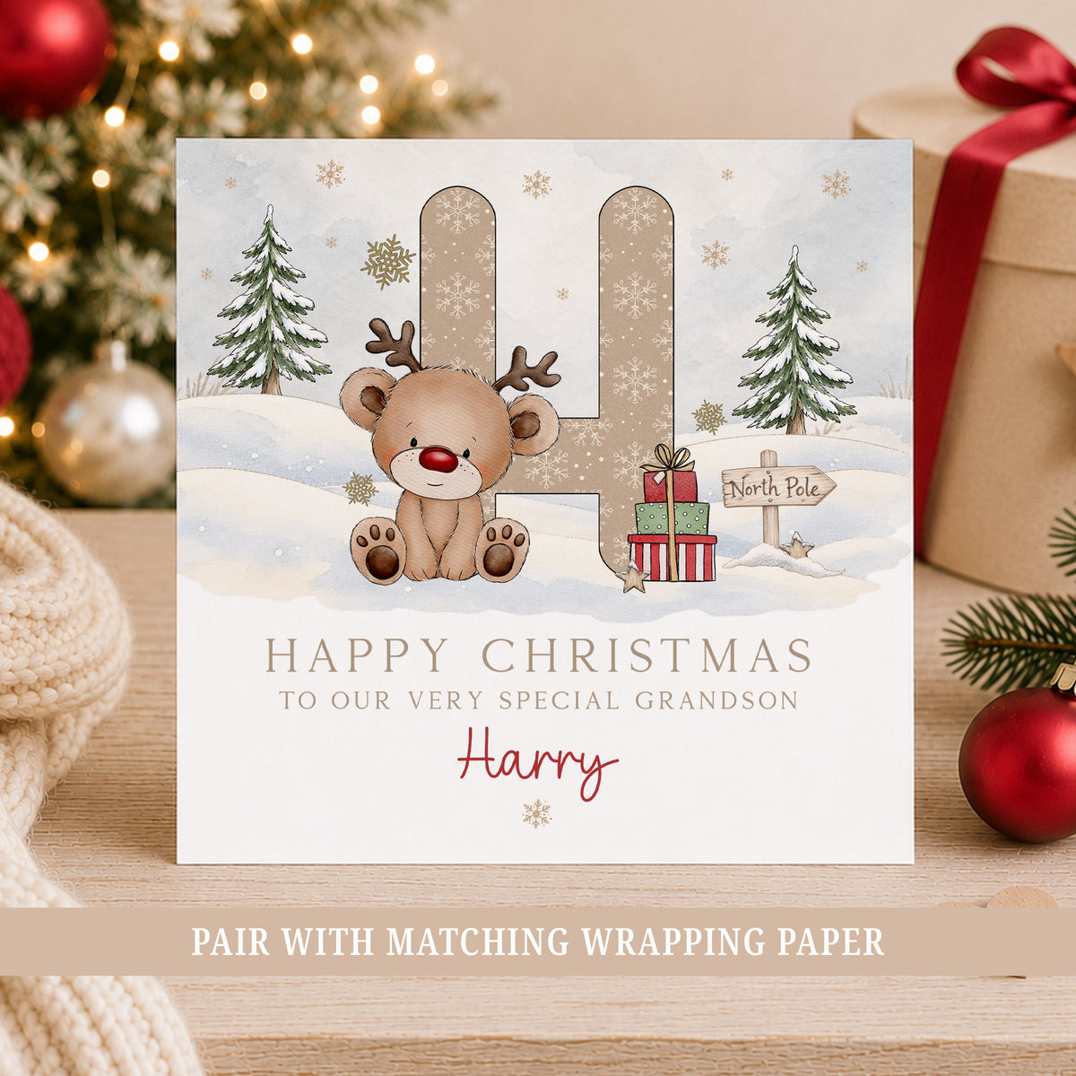 Personalised Grandson Christmas greeting card featuring a cute brown reindeer with antlers and a red nose, sitting in front of a large initial decorated with white snowflakes. The winter design includes snow-covered Christmas trees, festive presents, gold snowflakes and a wooden North Pole sign. Personalised with the child's initial, name and relation, this Christmas card is also suitable for a Son, Nephew or Little Boy.
