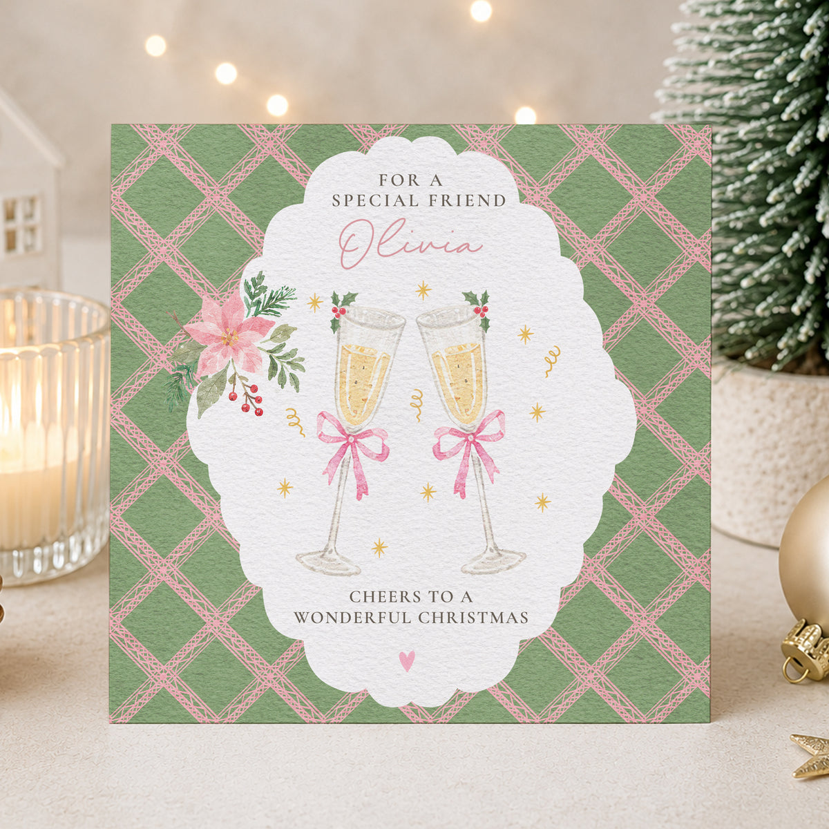 Personalised Friend Christmas card featuring two champagne glasses with pink bows, festive flowers and a green and pink patterned background. Personalised with the name Olivia and the wording Cheers to a Wonderful Christmas.