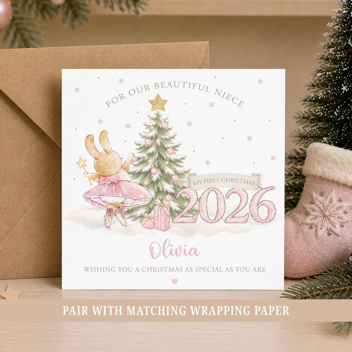 Personalised Granddaughter First Christmas 2026 greeting card featuring a sweet watercolour ballerina bunny in a pink tutu decorating a snowy Christmas tree with pink baubles and a gold star. The design includes pink Christmas presents, delicate snowflakes, a large pink 2026 and a First Christmas banner, with personalised name and relation wording. Also suitable for a Daughter, Niece or Baby Girl celebrating her first Christmas.