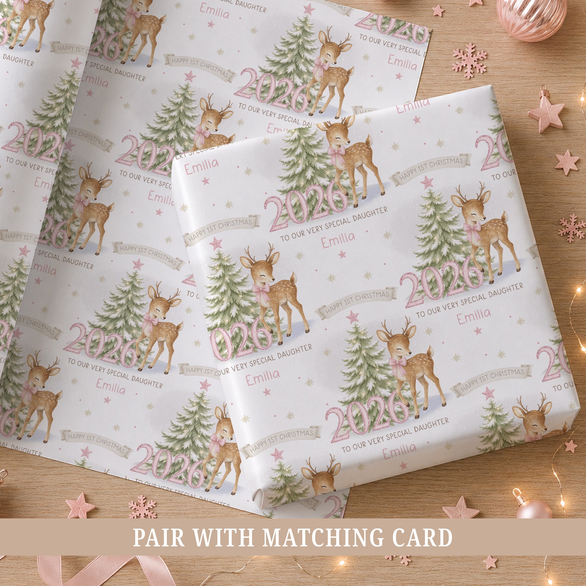Personalised baby girl First Christmas wrapping paper featuring a reindeer with pink bow, snowy Christmas tree, pink 2026 numbers, stars and snowflakes.