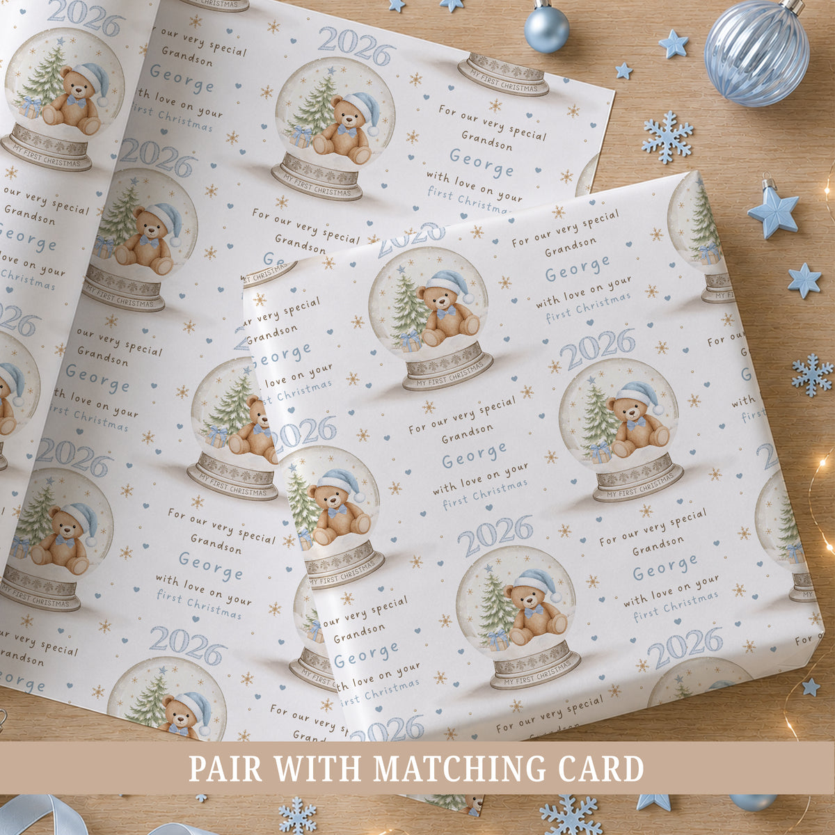 Personalised blue first Christmas wrapping paper featuring a teddy bear in a Christmas snow globe with blue hearts, gold snowflakes and the child’s name, relation and year.