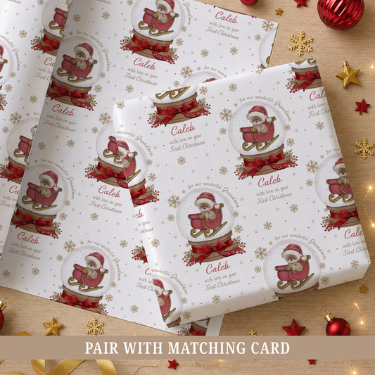 Personalised Grandson First Christmas wrapping paper featuring a teddy bear in a red sleigh inside a Christmas snow globe, with red bows, berries and gold snowflakes. Personalised with a name, relation and year and suitable for Grandson, Son, Nephew or Godson.
