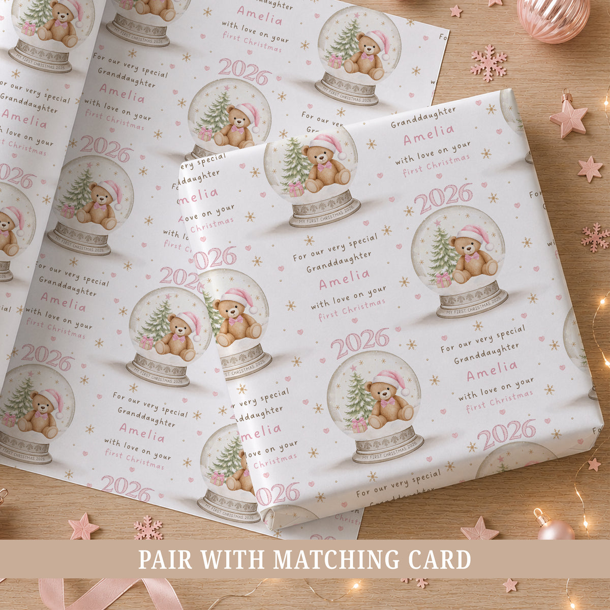 Personalised pink first Christmas wrapping paper featuring a teddy bear in a Christmas snow globe with pink hearts, snowflakes and the child’s name, relation and year.
