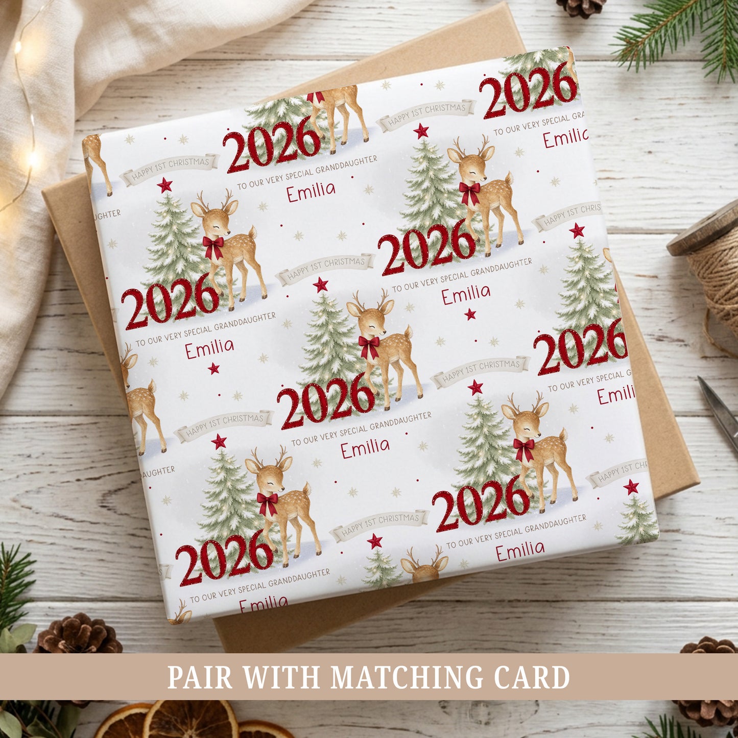 Personalised First Christmas wrapping paper featuring a sweet reindeer with red bow, snowy Christmas tree, red 2026 numbers, stars and snowflakes.