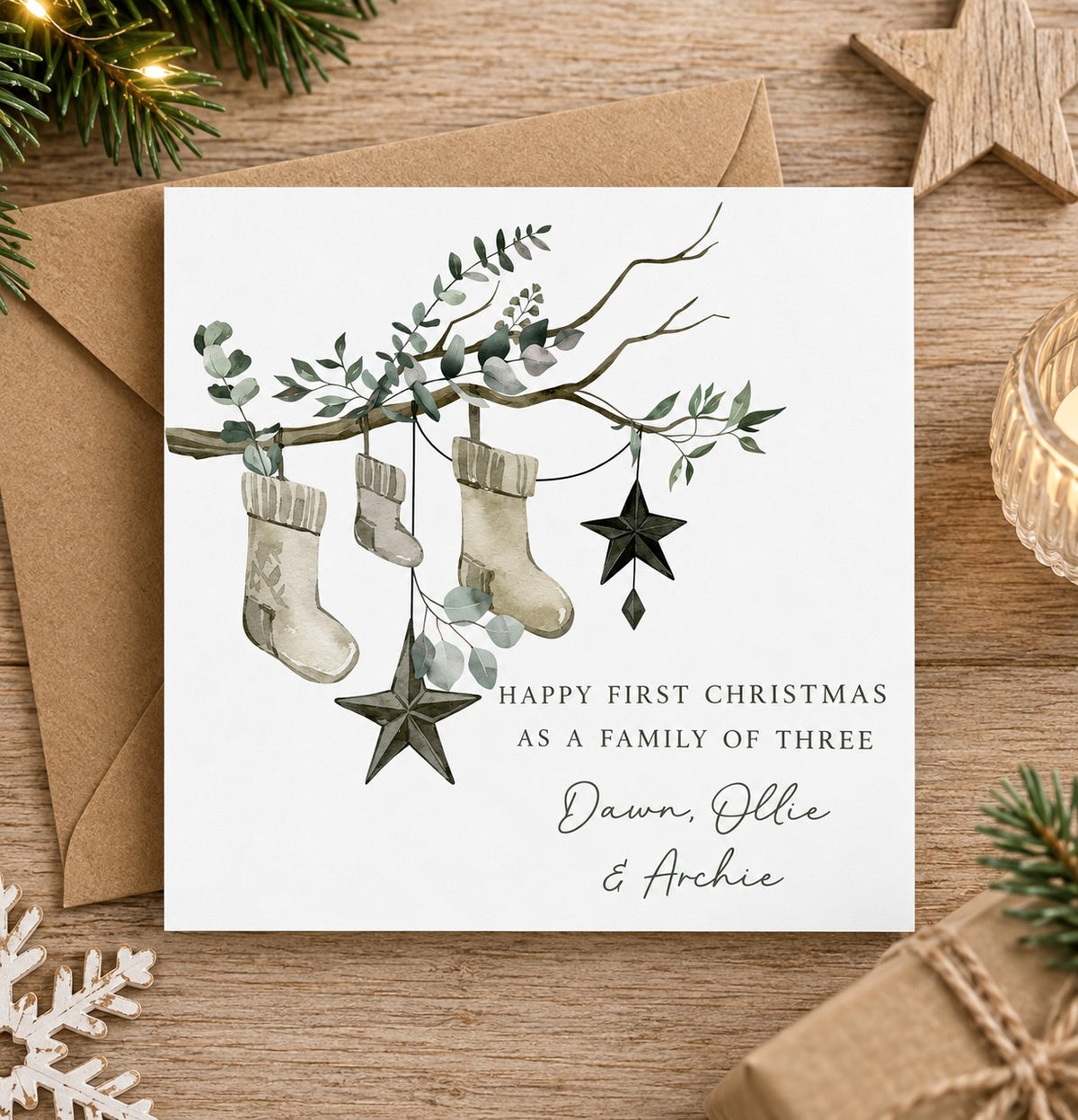 Personalised first Christmas as a family of three card featuring three festive stockings hanging from a eucalyptus branch with star decorations and personalised family names.
