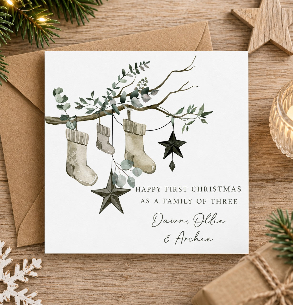 Personalised first Christmas as a family of three card featuring three festive stockings hanging from a eucalyptus branch with star decorations and personalised family names.