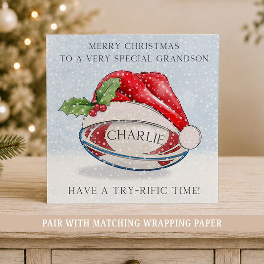 Personalised rugby Christmas card for boys featuring a rugby ball in a festive Santa hat, snowy blue background, child’s name.
